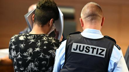 Einer von elf Angeklagten wird vor dem Prozessbeginn von einem Justizbeamten in einen Gerichtssaal im Landgericht gebracht. 