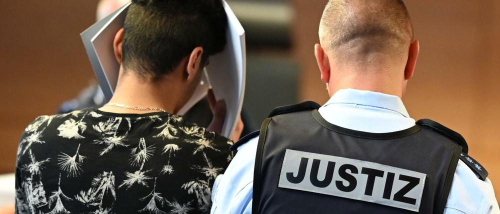 Einer von elf Angeklagten wird vor dem Prozessbeginn von einem Justizbeamten in einen Gerichtssaal im Landgericht gebracht.