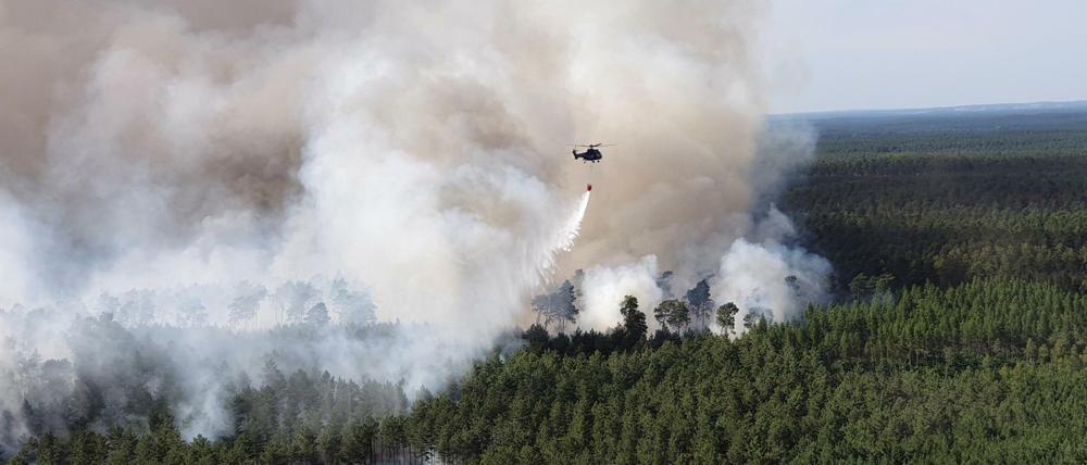 Ein Hubschrauber der Bundespolizei fliegt bei Löscharbeiten über einem Waldstück in der Lieberoser Heide.