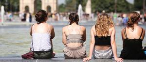 Vier Frauen sitzen bei heißen Temperaturen am Louvre auf dem Beckenrand eines Springbrunnens