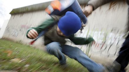 Ein Schüler drückt auf dem Schulhof eines Gymnasiums einen anderen Schüler zu Boden (gestelltes Illustrationsfoto).