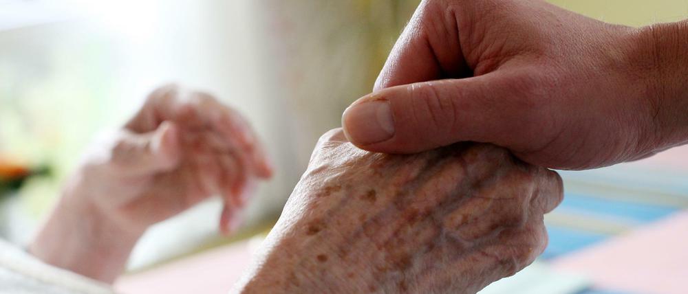 Ein Pfleger hält die Hand der Bewohnerin eines Pflegeheimes.