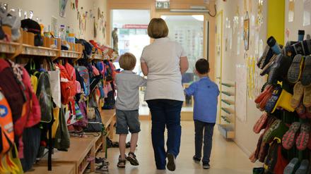 Eine Erzieherin geht im Kindergarten mit zwei Kindern über den Flur der Einrichtung.