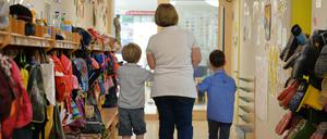 Eine Erzieherin geht im Kindergarten mit zwei Kindern über den Flur der Einrichtung.