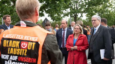 Svenja Schulze und Jörg Steinbach (r, beide SPD) werden von Helmar Rendez (l) und von Demonstranten in orangenen Westen empfangen. 