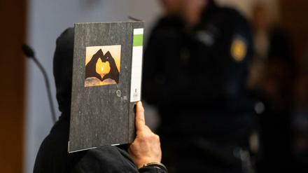 Der 58-jährige Angeklagte hält im Gerichtssaal einen Aktenordner mit einem Herz aus zwei Händen vor sein Gesicht