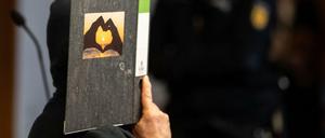 Der 58-jährige Angeklagte hält im Gerichtssaal einen Aktenordner mit einem Herz aus zwei Händen vor sein Gesicht