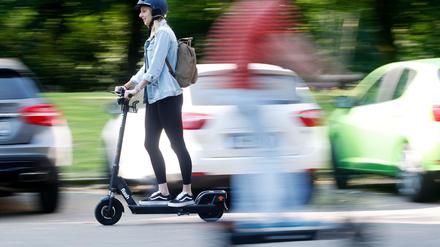 Frau fährt auf E-Scooter vor parkenden Autos.