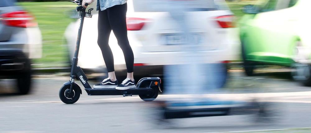 Frau fährt auf E-Scooter vor parkenden Autos.
