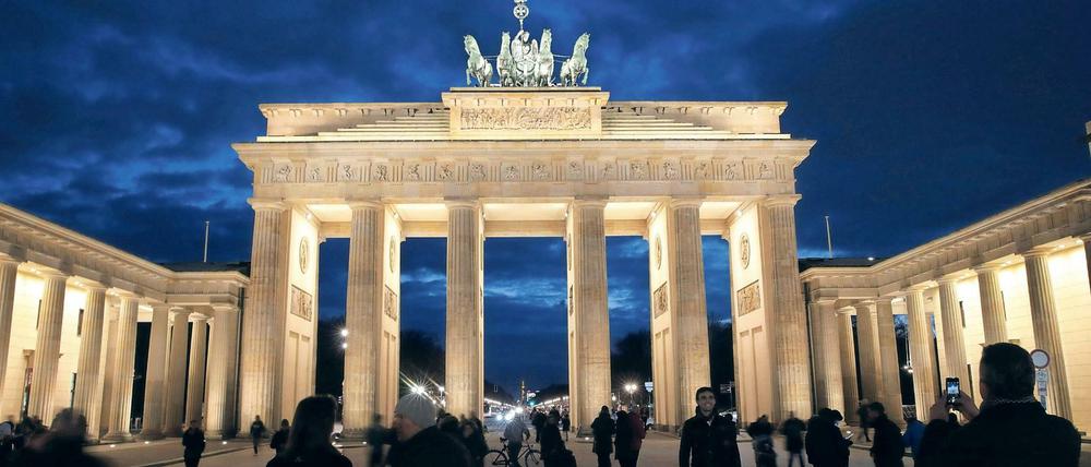Passanten gehen im Abendlicht vor dem Brandenburger Tor in Berlin spazieren.