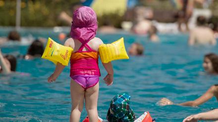 Ein Mädchen steht im Rheinbad in Düsseldorf mit seinen gelben Schwimmflügeln am Beckenrand.