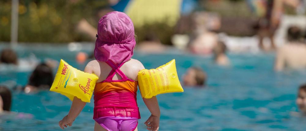 Ein Mädchen steht im Rheinbad in Düsseldorf mit seinen gelben Schwimmflügeln am Beckenrand.