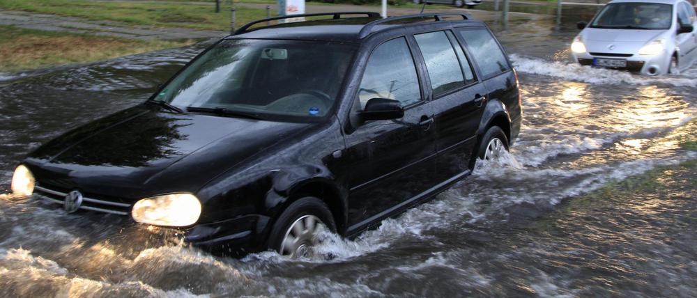 Berlin: Mehrere Autos fahren nach schweren Regenfällen über eine teilweise überflutete Straße.