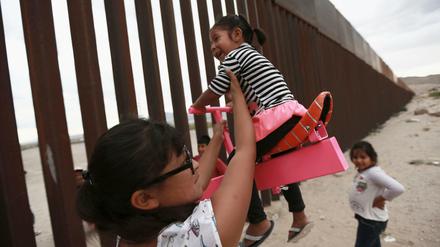 28.07.2019, Mexiko, Ciudad Juarez: Eine Frau spielt mit Mädchen an einer Wippe, die am Grenzzaun zwischen Mexiko und den USA angebracht ist. Die Wippe wurde von Ronald Rael, einem Professor für Architektur in Kalifornien, entworfen.