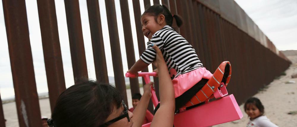 28.07.2019, Mexiko, Ciudad Juarez: Eine Frau spielt mit Mädchen an einer Wippe, die am Grenzzaun zwischen Mexiko und den USA angebracht ist. Die Wippe wurde von Ronald Rael, einem Professor für Architektur in Kalifornien, entworfen.