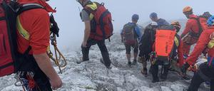 Bergretter transportieren in dichtem Nebel eine zuvor am Watzmann abgestürzte Bergsteigerin auf einer Trage den Berg hinunter. 