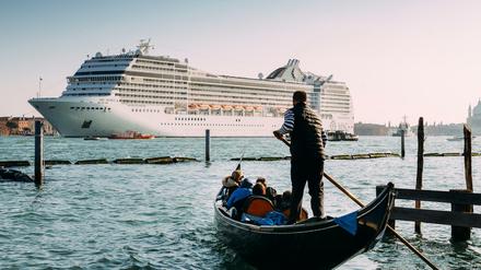 Zwischen Romantik und Massentourismus. Ein Gondoliere führt einige Urlauber durch die Kanäle von Venedig, während ein Kreuzfahrtschiff in die Lagune einfährt. 