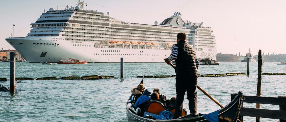 Zwischen Romantik und Massentourismus. Ein Gondoliere führt einige Urlauber durch die Kanäle von Venedig, während ein Kreuzfahrtschiff in die Lagune einfährt.