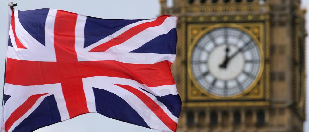Großbritannien, London: Eine britische Fahne weht vor dem berühmten Uhrturm Big Ben.