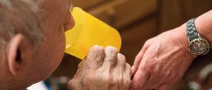Eine ambulante Pflegerin hilft einem alten Mann bei der Tabletteneinnahme, der Mann trinkt Wasser.