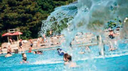 Kinder spielen im Freibad Prinzenbad in Berlin unter pilzförmigen Brunnen.