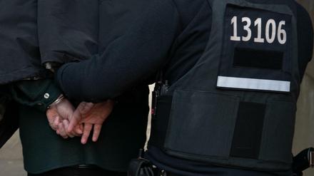 Berlin: Polizeibeamte führen mit Handschellen einen festgenommenen Mann nach einer Razzia in einem Wohnhaus in Tempelhof ab.