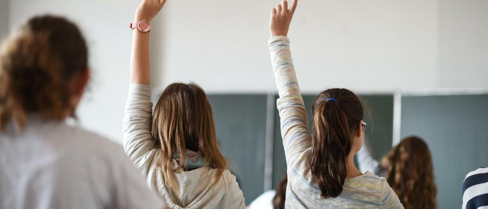 In einer Schulklasse melden sich Schülerinnen im Unterricht.