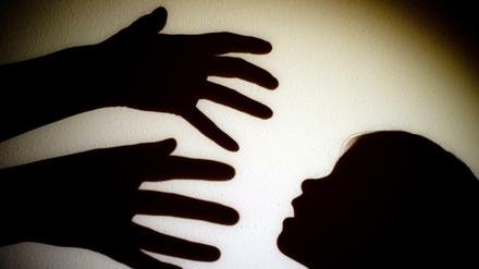 Schatten von Händen einer erwachsenen Person und dem Kopf eines Kindes an einer Wand eines Zimmers. 