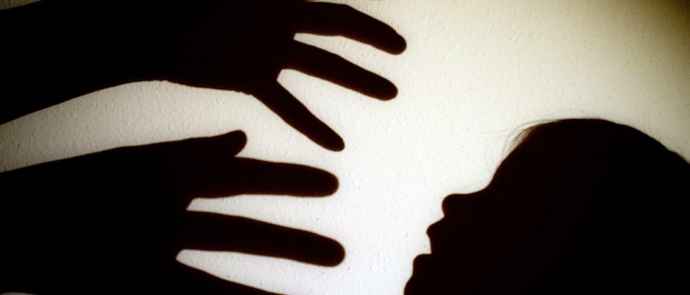 Schatten von Händen einer erwachsenen Person und dem Kopf eines Kindes an einer Wand eines Zimmers.