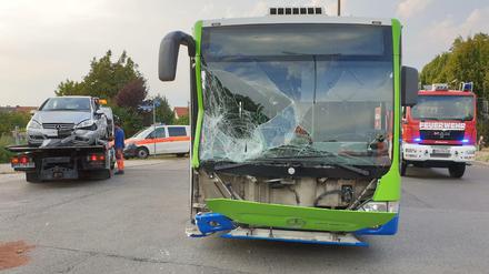 Ein Schulbus steht nach einem Unfall beschädigt auf der Straße, während ein Fahrzeug abgeschleppt wird. 