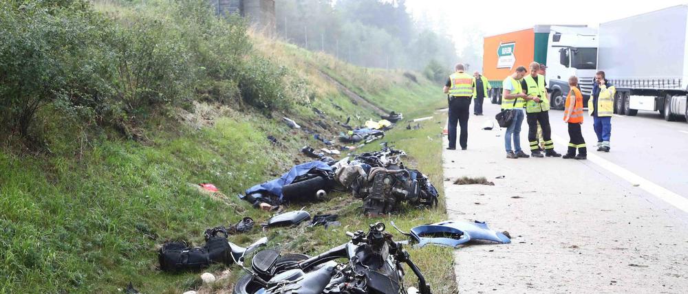 Thüringen, Bad Lobenstein: Einsatzkräfte stehen an einer Unfallstelle auf der A 9, Motorräder und Trümmerteile liegen neben der Fahrbahn an der Böschung.