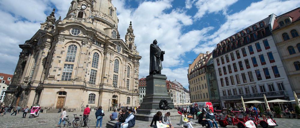 Vor dem Martin-Luther-Standbild auf dem Neumarkt in Dresden (Sachsen) rasten am Touristen, links die Frauenkirche.