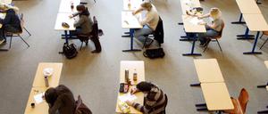 Schülerinnen und Schüler sitzen bei einer Abiturprüfung an Einzeltischen.