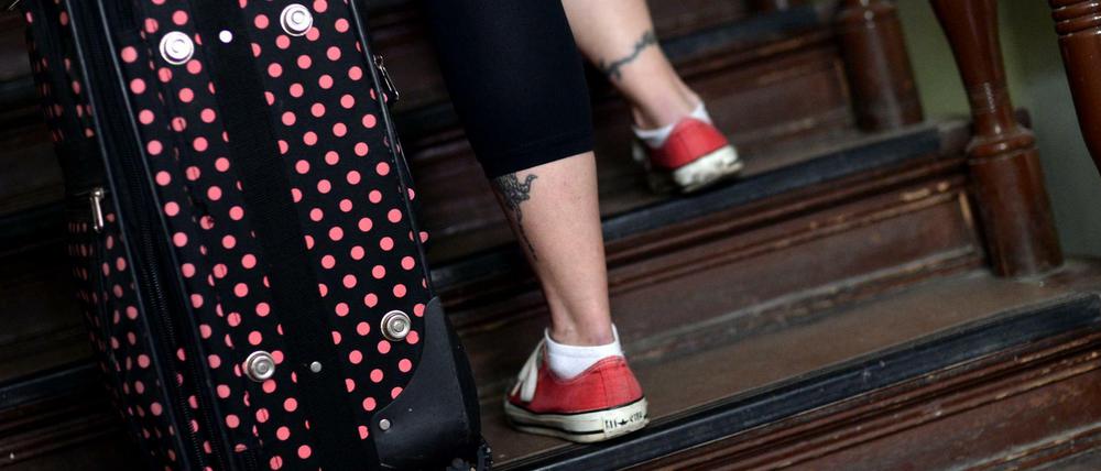 Eine junge Frau geht in Berlin mit einem Rollkoffer die Treppe eines Mietshauses herauf. 