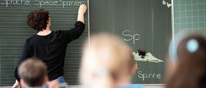 Eine Grundschullehrerin schreibt Wörter an eine Tafel, die Kinder folgen dem Unterricht.
