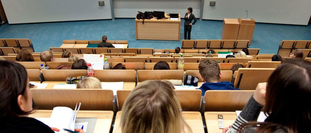 Studierende sitzen in einem Hörsaal, vor ihnen steht eine Lehrende.