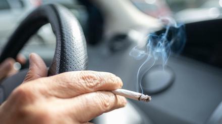 Ein Mann sitzt rauchend am Lenkrad eines Autos.
