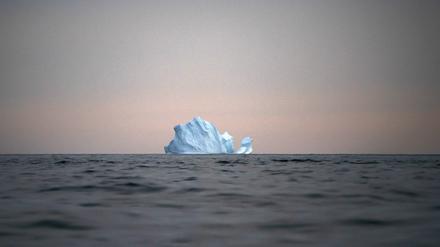 Grönland, Kulusuk: Ein Eisberg schwimmt bei Sonnenuntergang auf dem Meer.
