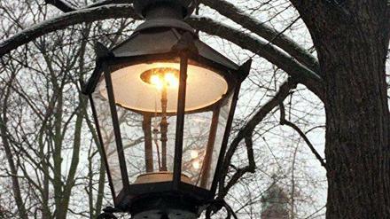 Brennende Gaslaterne vor winterlicher Baumkulisse.