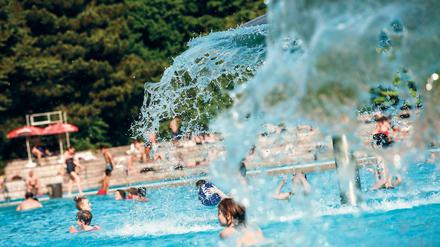 Kinder spielen im Freibad Prinzenbad in Berlin unter pilzförmigen Brunnen.