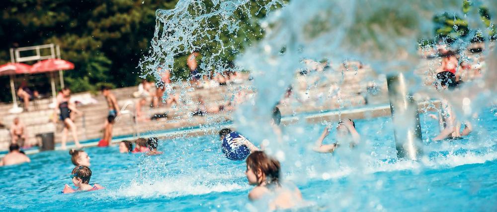 Kinder spielen im Freibad Prinzenbad in Berlin unter pilzförmigen Brunnen.