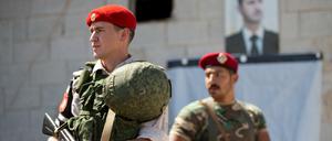 Russische und syrische Militärpolizisten stehen Wache vor einem Porträt des syrischen Präsidenten al-Assad. 