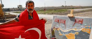 Ein Mann mit einer türkischen Flagge steht an der Grenze zwischen der Türkei und Syrien neben einer Karte, welche die geplante militärische Operation der Türkei in Syrien zeigt.