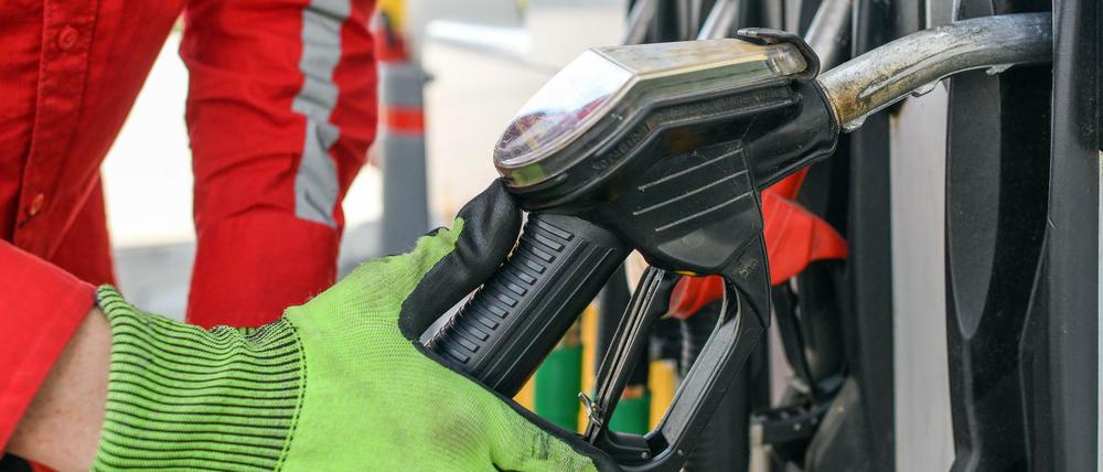Ein Tankwart nimmt eine Zapfpistole aus der Halterung einer Zapfsäule einer Tankstelle.