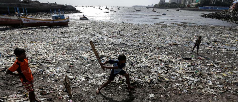 Kinder spielen an einem vermüllten Strand in Mumbai Cricket.