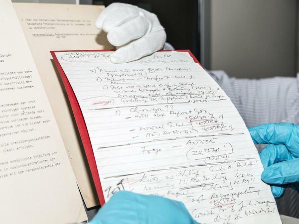 Mit Handschuhen heben Mitarbeiter Schabowskis Zettel hoch.