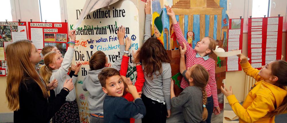 Schülerinnen und Schüler der Grunewald-Schule reißen das Papier ab, mit dem zwei Mauer-Dominosteine verhüllt waren.