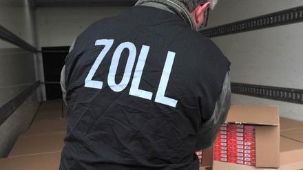 Ein Zollbeamter kontrolliert Kartons mit sichergestellten Zigarettenstangen (Symbolbild).