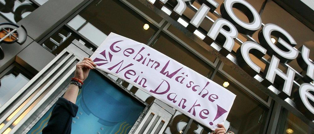 Eröffnung in Berlin 2007. Eine Frau protestiert vor der Scientology-Dependance mit einem Schild "Gehirnwäsche - Nein Danke !".