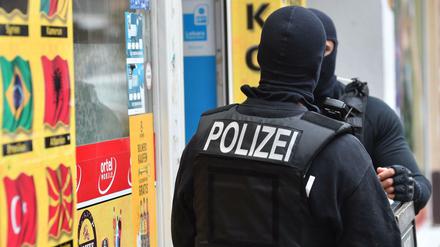 Vermummte Einsatzkräfte stehen vor einem Kiosk im Stadtteil Neukölln. 